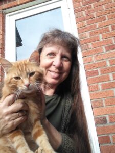 a woman holding an orange cat in front of a glass door and brick building.